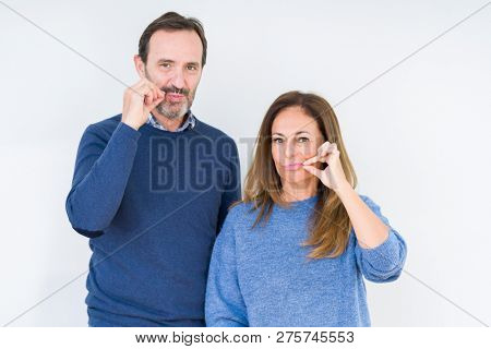 Beautiful middle age couple in love over isolated background mouth and lips shut as zip with fingers. Secret and silent, taboo talking