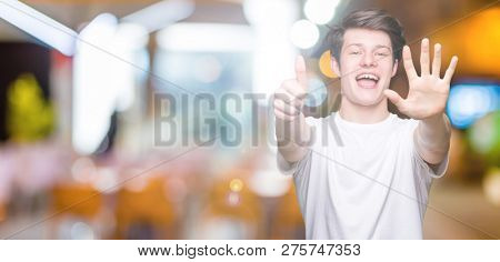 Young handsome man wearing casual white t-shirt over isolated background showing and pointing up with fingers number six while smiling confident and happy.