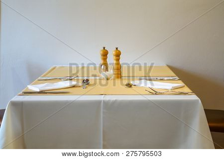 Minimalistic Table In Restaurant With Plain Table Cloth, Cutlery, Napkins And Salt And Pepper Mills 