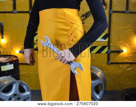 Fashionable Mechanic Girl In Trendy Clothes Is Holding A Wrench On The Background Of The Workshop Of