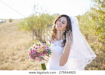 Beautiful Smiling Bride Wearing A Natural Flower Wreath And Standing In The Golden Summer Fields Wit