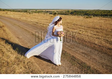 Beautiful Smiling Bride Wearing A Natural Flower Wreath And Standing In The Golden Summer Fields Wit