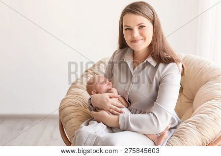 Young Mother With Her Newborn Baby In Papasan Chair At Home