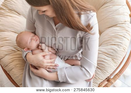 Young Mother With Her Newborn Baby In Papasan Chair At Home