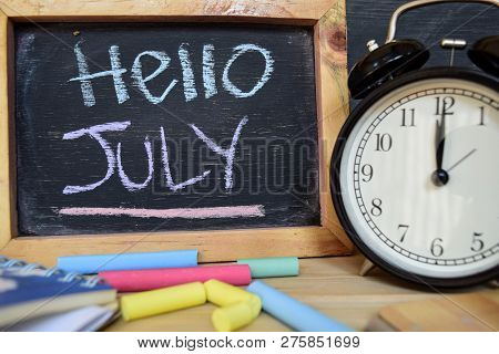 Hello July. Back To School Concept. Alarm Clock On Wooden With Blackboard On Background