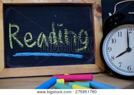 Reading. Back To School Concept. Alarm Clock On Wooden With Blackboard On Background