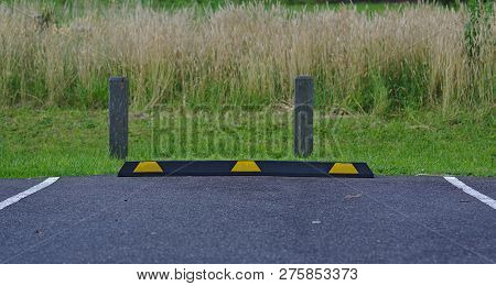 Rubber Parking Block In Black And Yellow Colors On Asphalt Surface With Wild Grass Background