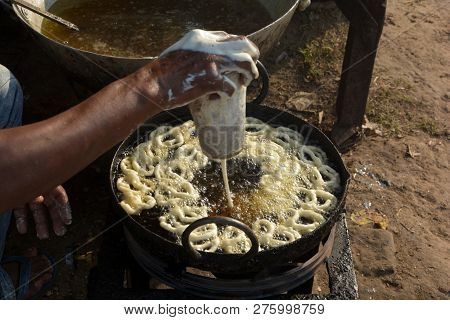 Close Of A Hand Frying Jalebi In Hot Oil In A Street Village Market In A Stove In Daylight