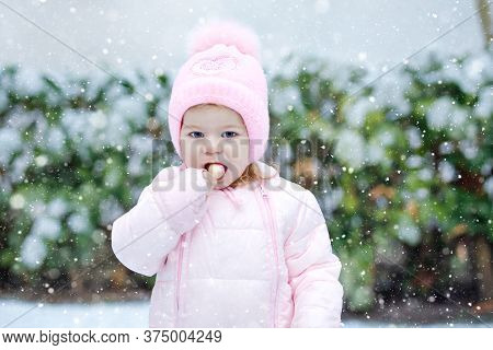 Portrait Of Little Toddler Girl Walking Outdoors In Winter. Cute Toddler Eating Sweet Lollypop Candy