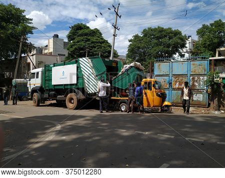 Closeup Of Garbage Collecting Workers Working To Unload Waste From Auto To Lorry In A Roadside.