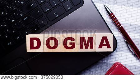 The Word Dogma Is Written On Wooden Cubes That Stand On The Keyboard Near The Pen