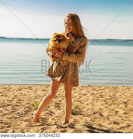 Portrait Of Beautiful Red-haired Girl 10 Years Old Sits On A Sandy Beach Near Water With Wonderful P