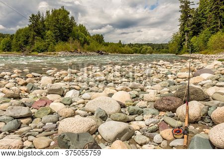 Fly Rod Resting On Boulders Beside The Fast Flowing Kitimat River In British Columbia, Canada.