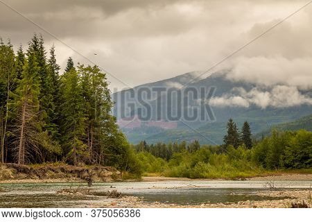 Landscape Of A River, Mountain And Forest, With An Eagle In The Sky, During A Cloudy Summer Day, On 