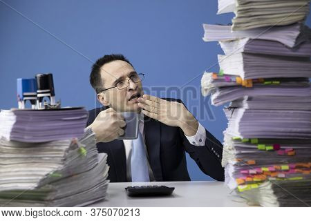Exhausted Office Worker Yawns Tired Of Looking At Huge Stack Of Documents. Fatigue And Overload Conc