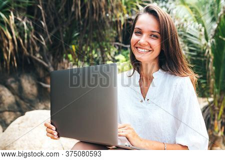 Young Girl, A Business Lady Working On A Laptop While Traveling Sitting Among Tropical Palm Trees On