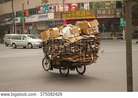 Chinese Man Riding A Cargo Tricycle Loaded With Cardboard Waste On A Road In China. Cargo Bikes Or F