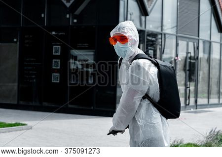 Man Riding Electric Kick Scooter Near Modern Buildings And Wearing Anti Covid Protective Suit, Glass