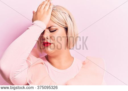 Beautiful blonde plus size woman wearing pincess tiara with diamonds over pink background surprised with hand on head for mistake, remember error. Forgot, bad memory concept.