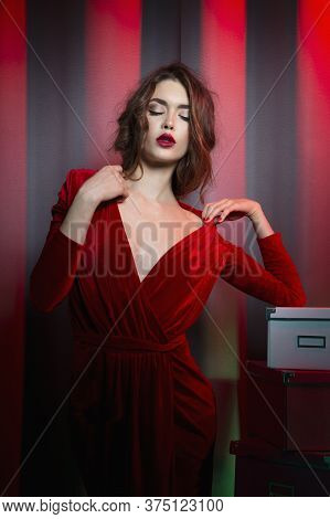 Gorgeous Brunette Woman In Elegant Velvet Red Dress With Decolletage, Posing In Studio At The Red Ne