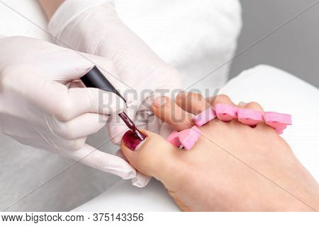 Hands In Protective Gloves Painting Red Nail Polish On Female Toenail In Beauty Salon