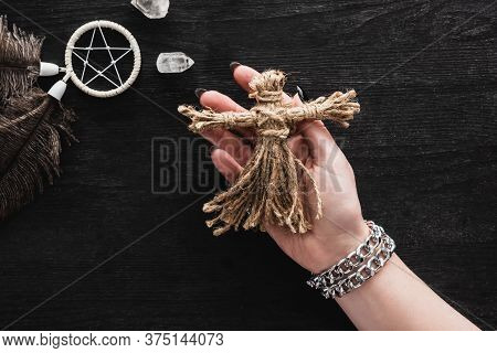 Top View Of Woman Holding Voodoo Doll Near Pentagram And Crystals On Black