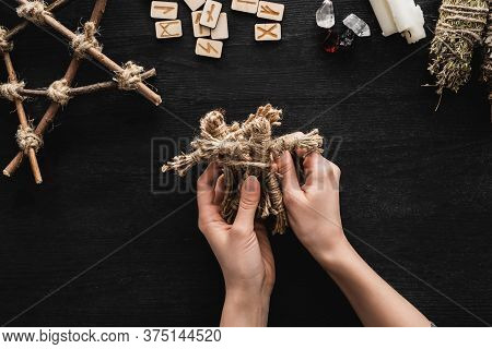 Top View Of Woman Holding Voodoo Dolls Near Scandinavian Runes, Pentagram, Candles And Crystals On B