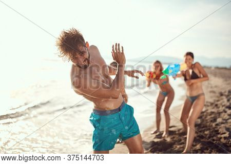 women sprinkle beardy guy with water guns on beach. copy space