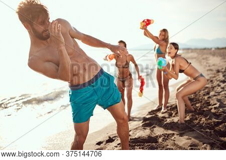 three women sprinkle beardy guy with water guns on sandy beach