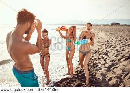 women sprinkle beardy guy with water guns on sandy beach