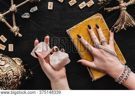 Top View Of Witch Holding Crystals And Touching Aged Book Of Dark Magic Near Voodoo Doll And Runes O