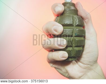 The Hand Holds An Old Soviet Grenade On A Pink Background. Closeup Photo