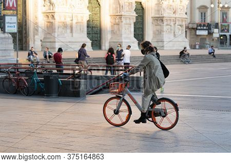 Milan, Italy - May 4, 2020: Woman Riding Bicycle Through Duomo Square. Italy Enters Second Phase Of 