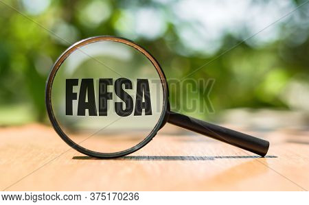Free Application For Federal Student Aid - Fafsa Written On Magnifying Glass On Wooden Table And Gre