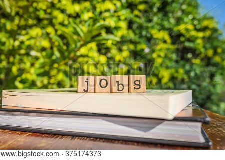 The Word Jobs, Letters On Block Cubes On Top Of Books And Wooden Table With Green Trees, Outdoor Nat