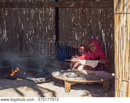 Bedouin Village In Desert, Egypt - February 2020: Two Arabian Girls Preparing Food Near Fireplace, M