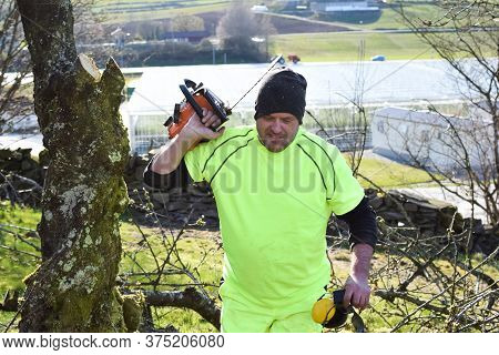 Worker In The Garden With A Chainsaw.