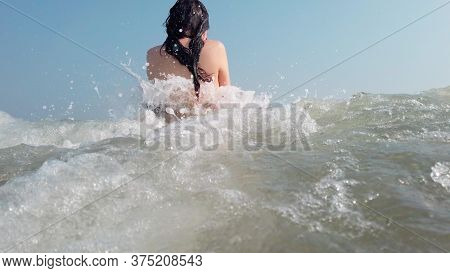 A Young Woman In A Black Swimsuit Spends Time In The Sea Or Ocean. The Girl Takes Refuge From The Wa