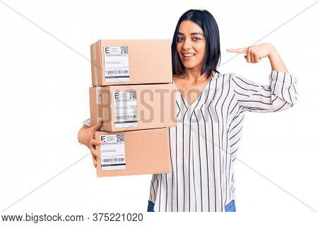 Young beautiful latin woman holding delivery package pointing finger to one self smiling happy and proud 