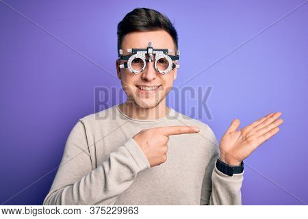 Young handsome caucasian man wearing optometrical glasses over purple background amazed and smiling to the camera while presenting with hand and pointing with finger.