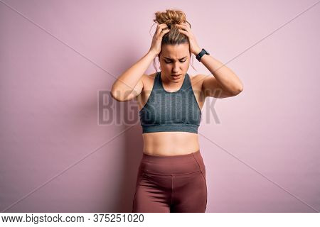 Young beautiful blonde sportswoman doing sport wearing sportswear over pink background suffering from headache desperate and stressed because pain and migraine. Hands on head.