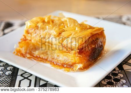 Delicious Greek sweet pastry named Galaktoboureko, made of semolina custard in filo, served with honey in white plate.