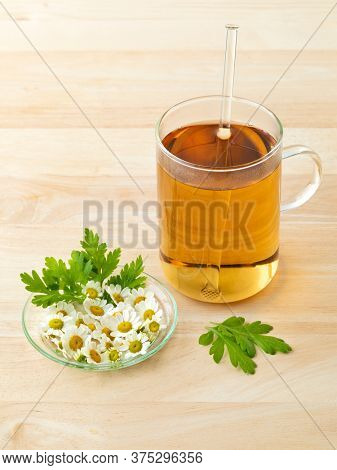 Glass of herbal tea with fresh Feverfew flowers on a dish 