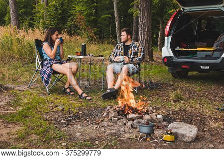 Couple Sitting In Portable Chairs Drinking Tea Talking. Camping Summer Activities