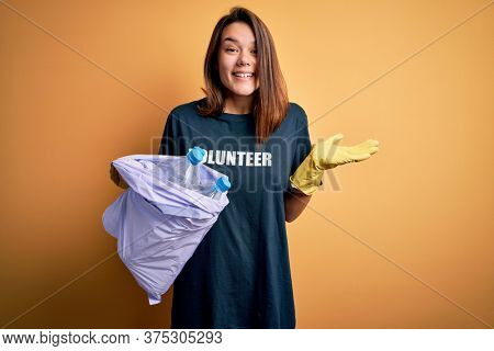Beautiful volunteer girl caring environment doing volunteering holding bag with rubish bottles very happy and excited, winner expression celebrating victory screaming with big smile and raised hands