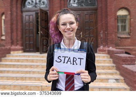 Female Student Teenager With Notepad And Handwritten Word Start, School Building Background. Back To