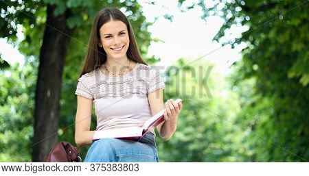 Beautiful female college student reading a book on a bench in a park