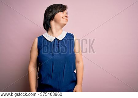 Young down syndrome woman wearing elegant shirt over pink background looking away to side with smile on face, natural expression. Laughing confident.