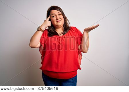 Beautiful brunette plus size woman wearing casual red t-shirt over isolated white background confused and annoyed with open palm showing copy space and pointing finger to forehead. Think about it.