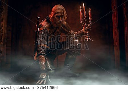 Scenic portrait of a brave medieval warrior in armor and with a sword. The Witcher man.